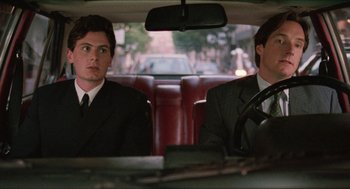 Movie still from “Barcelona” (1994), directed by Whit Stillman – Two men in suits sitting in the back seat of a car; Medium shot, Over the shoulder angle