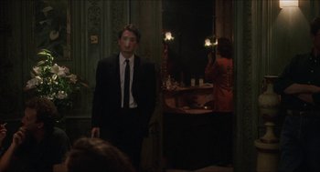 Movie still from “Barcelona” (1994), directed by Whit Stillman – A man in a suit and tie standing in front of a mirror; Medium shot, Over the shoulder angle