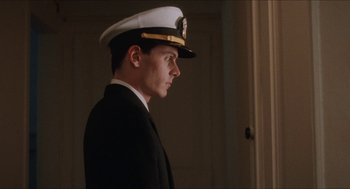 Movie still from “Barcelona” (1994), directed by Whit Stillman – A man in a naval uniform standing next to a door; Medium shot, Low angle