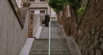 Movie still from “Barcelona” (1994), directed by Whit Stillman – A man walking up a set of stairs with a guitar; Extreme Wide shot, Low angle
