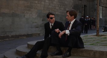 Movie still from “Barcelona” (1994), directed by Whit Stillman – A couple of men sitting on top of a step outside; Medium shot, Over the shoulder angle