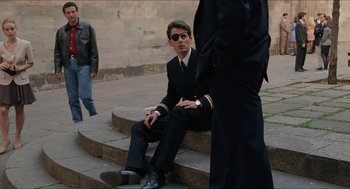 Movie still from “Barcelona” (1994), directed by Whit Stillman – A man sitting on steps wearing a suit and tie; Wide shot, Over the shoulder angle