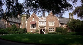 Movie still from “Batman: The Movie” (1966), directed by Leslie H. Martinson – Two people are standing in front of a large brick house; Extreme Wide shot, Low angle