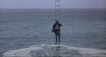 Movie still from “Batman: The Movie” (1966), directed by Leslie H. Martinson – A man standing in the ocean holding onto a ladder; Wide shot, High angle