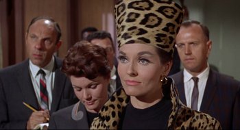 Movie still from “Batman: The Movie” (1966), directed by Leslie H. Martinson – A group of people in a room with a woman wearing a leopard print hat; Close Up shot, Low angle