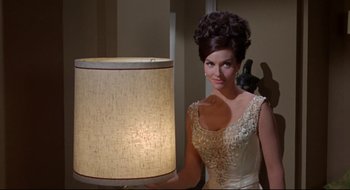 Movie still from “Batman: The Movie” (1966), directed by Leslie H. Martinson – A woman standing next to a lamp in a room; Medium shot, Low angle