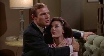 Movie still from “Batman: The Movie” (1966), directed by Leslie H. Martinson – A man and a woman hugging each other in front of a couch; Close Up shot, Low angle