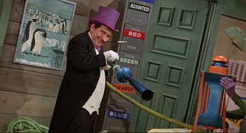 Movie still from “Batman: The Movie” (1966), directed by Leslie H. Martinson – A man in a purple top hat and white gloves is holding a blue hose; Medium shot, Low angle