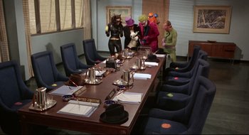 Movie still from “Batman: The Movie” (1966), directed by Leslie H. Martinson – A group of people dressed up in costumes around a long table; Wide shot, High angle