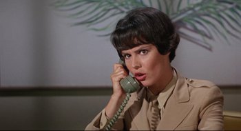 Movie still from “Batman: The Movie” (1966), directed by Leslie H. Martinson – A woman talking on a phone while wearing a suit and tie; Close Up shot, Low angle
