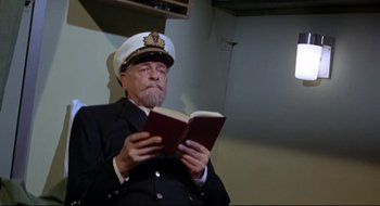 Movie still from “Batman: The Movie” (1966), directed by Leslie H. Martinson – An older man in a uniform reading a book; Medium shot, High angle