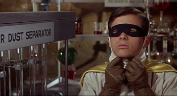 Movie still from “Batman: The Movie” (1966), directed by Leslie H. Martinson – A man wearing a black mask and gloves in a lab; Medium shot, Low angle