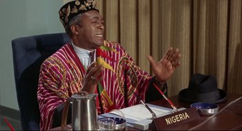 Movie still from “Batman: The Movie” (1966), directed by Leslie H. Martinson – A man in a red and yellow striped robe sitting at a table; Medium shot, Low angle