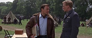 Movie still from “The Battle of Britain” (1969), directed by Guy Hamilton – A man in a brown jacket talking to another man in a brown jacket; Medium shot, Over the shoulder angle