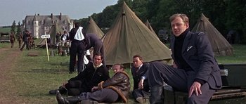 Movie still from “The Battle of Britain” (1969), directed by Guy Hamilton – A group of men sitting on the ground in front of tents; Medium shot, Over the shoulder angle