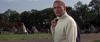 Movie still from “The Battle of Britain” (1969), directed by Guy Hamilton – A man in a white sweater holding a microphone in a field; Close Up shot, Low angle