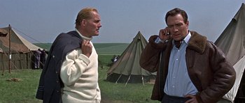 Movie still from “The Battle of Britain” (1969), directed by Guy Hamilton – Two men standing next to each other in front of a tent; Medium shot, Low angle