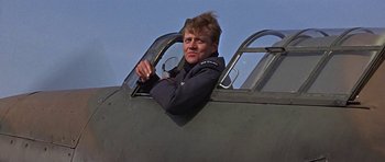 Movie still from “The Battle of Britain” (1969), directed by Guy Hamilton – A man sitting inside of an old fighter plane; Medium shot, Low angle