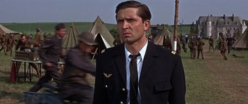 Movie still from “The Battle of Britain” (1969), directed by Guy Hamilton – A man in a suit and tie standing in front of tents; Close Up shot, Low angle