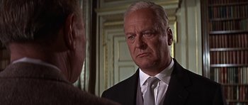 Movie still from “The Battle of Britain” (1969), directed by Guy Hamilton – An older man wearing a suit and tie in front of another man; Close Up shot, Over the shoulder angle