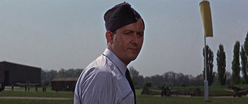 Movie still from “The Battle of Britain” (1969), directed by Guy Hamilton – A man wearing a hat and a tie in a field; Close Up shot, Low angle