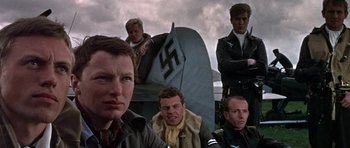 Movie still from “The Battle of Britain” (1969), directed by Guy Hamilton – A group of men standing next to each other in front of an airplane; Close Up shot, Low angle