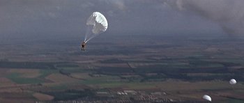 Movie still from “The Battle of Britain” (1969), directed by Guy Hamilton – A person is parachuting in the air over a field; Extreme Wide shot, High angle