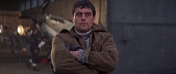 Movie still from “The Battle of Britain” (1969), directed by Guy Hamilton – A man with his arms crossed wearing a brown jacket; Close Up shot, Low angle