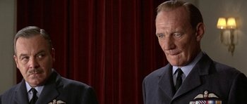 Movie still from “The Battle of Britain” (1969), directed by Guy Hamilton – A man in a suit and tie standing next to another man in a suit and tie; Close Up shot, Over the shoulder angle