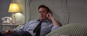 Movie still from “The Battle of Britain” (1969), directed by Guy Hamilton – A man sitting in a bed wearing a neck tie; Medium shot, Low angle