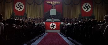 Movie still from “The Battle of Britain” (1969), directed by Guy Hamilton – A crowd of people sitting in front of a podium with a nazi flag on it; Extreme Wide shot, High angle
