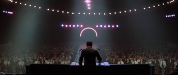 Movie still from “The Battle of Britain” (1969), directed by Guy Hamilton – A man standing in front of an audience in front of lights; Wide shot, Low angle