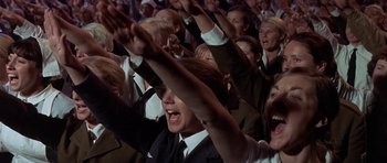 Movie still from “The Battle of Britain” (1969), directed by Guy Hamilton – A group of people in suits raising their hands in the air; Medium shot, High angle