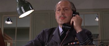 Movie still from “The Battle of Britain” (1969), directed by Guy Hamilton – An older man in a uniform talking on a phone; Close Up shot, Low angle