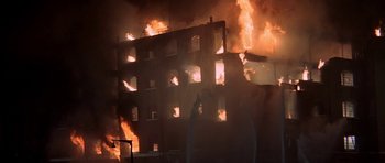Movie still from “The Battle of Britain” (1969), directed by Guy Hamilton – A building that is on fire with smoke billowing out of it; Extreme Wide shot, Low angle