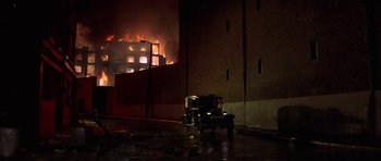 Movie still from “The Battle of Britain” (1969), directed by Guy Hamilton – An old car parked in front of a building on fire at night; Extreme Wide shot, Low angle