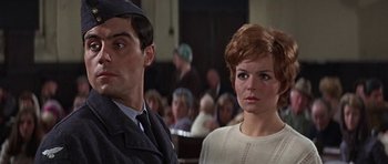 Movie still from “The Battle of Britain” (1969), directed by Guy Hamilton – A man and a woman are sitting in front of an audience; Close Up shot, Low angle