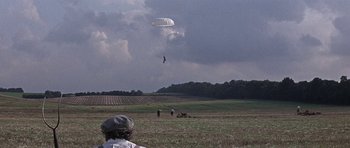 Movie still from “The Battle of Britain” (1969), directed by Guy Hamilton – A person is parachuted into the sky over a field; Extreme Wide shot, High angle