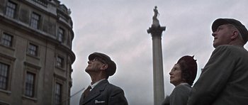 Movie still from “The Battle of Britain” (1969), directed by Guy Hamilton – A man and a woman standing in front of a statue; Medium shot, Low angle