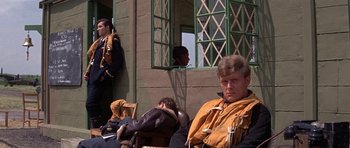 Movie still from “The Battle of Britain” (1969), directed by Guy Hamilton – A group of people sitting in front of a building; Medium shot, Low angle