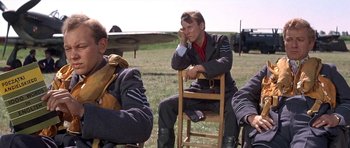 Movie still from “The Battle of Britain” (1969), directed by Guy Hamilton – A group of men sitting in a field next to an airplane; Medium shot, Low angle