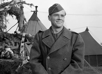 Movie still from “Battleground” (1949), directed by William A. Wellman – A man in a military uniform standing in front of tents; Medium shot, Low angle