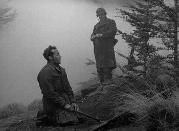 Movie still from “Battleground” (1949), directed by William A. Wellman – Two men are sitting on the ground and one of them is holding a rifle; Medium shot, Low angle