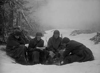 Movie still from “Battleground” (1949), directed by William A. Wellman – A black and white photo of a group of men sitting in the snow; Wide shot, High angle
