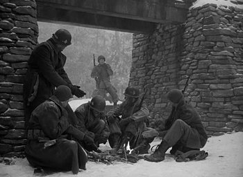 Movie still from “Battleground” (1949), directed by William A. Wellman – A black and white photo of soldiers sitting in the snow; Wide shot, High angle