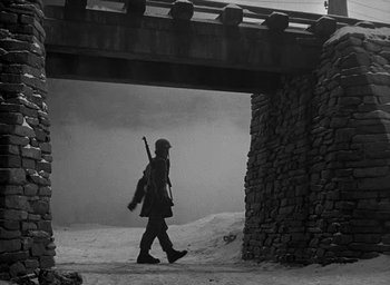 Movie still from “Battleground” (1949), directed by William A. Wellman – A man walking in the snow holding a rifle; Wide shot, Low angle