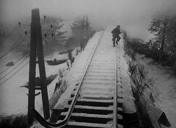 Movie still from “Battleground” (1949), directed by William A. Wellman – A man riding a snowboard down a snow covered slope; Extreme Wide shot, High angle