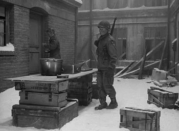 Movie still from “Battleground” (1949), directed by William A. Wellman – A man holding a rifle standing next to a pot on a table; Wide shot, High angle