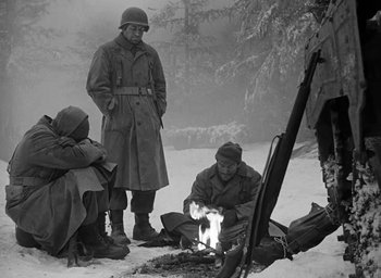 Movie still from “Battleground” (1949), directed by William A. Wellman – A black and white photo of a group of men sitting around a fire; Medium shot, High angle