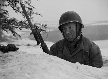 Movie still from “Battleground” (1949), directed by William A. Wellman – A man with a rifle standing next to a tree; Medium shot, Low angle